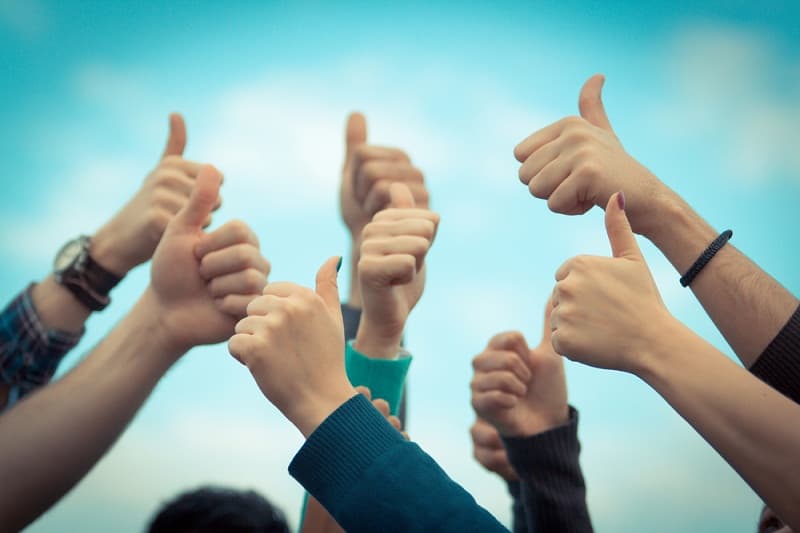 Several raised hands giving a thumbs-up against a blue sky